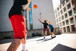 © Studio Marmellata - Three diverse players enjoy an energetic outdoor basketball game. One person passes the ball as two opponents reach to intercept it on a sunny urban court.