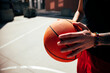 © Studio Marmellata - A young athlete holds a textured basketball firmly with both hands on an outdoor court. The person wears a black shirt and red shorts, showcasing a casual, active lifestyle.