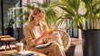 © ArtFocus Studio - Happy Young Businesswoman in Tan Suit Sitting on Wicker Chair and Using Smartphone on a Sunny Outdoor Terrace with Plants and Coffee