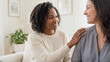 © alchena - Two adult women talk and support each other at home, showing empathy and trust. Multicultural friendship, emotional connection, care, mental health, communication and comfort indoors.