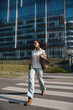 © verona_studio - Pretty Woman Running Across Crosswalk Near Modern Office Building Wearing Beige Blazer And Jeans. Casual Business Lifestyle Concept Female Urban