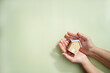 © Suraphol - Hands hold wooden house model on light green background. Real estate, buy and sale, Property insurance, property protection, real estate safety, and residential care.