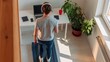 © oksa_studio - Woman wearing headphones is running on treadmill in front of her home office desk, combining fitness with work.