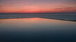© Lumi Stock Studio - Infinity edge pool with reflection of pink sunset sky over calm ocean horizon, luxury resort coastal escape with peaceful tranquil atmosphere