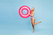 © ViDi Studio - Full body sideways young sexy fun woman she wears bikini swimsuit rest near hotel pool hold in hand pink rubber ring look camera isolated on plain blue background. Summer vacation sea sun tan concept.