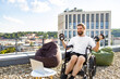 © sofiko14 - A man with a beard in a wheelchair is lifting dumbbells on a rooftop terrace with a city view, engaging in a fitness routine