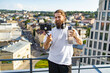 © sofiko14 - A bearded man with headphones around his neck films himself with a smartphone on a gimbal while holding a water bottle on a city rooftop