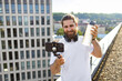 © sofiko14 - A smiling man with a beard and headphones around his neck holds a water bottle while recording a video on his smartphone mounted on a tripod