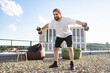 © sofiko14 - A bearded man with long hair tied back performs dumbbell exercises on a rooftop patio with beanbag chairs and a modern building in the background