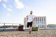 © sofiko14 - A man with a beard and tied-back hair performs a quadriceps stretch on a gravel rooftop with a modern building in the background