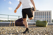 © sofiko14 - A man performs a quadriceps stretch on a gravel rooftop with beanbags and a modern building in the background