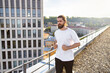 © sofiko14 - A man with a beard and bun hairstyle runs on a rooftop with a city skyline in the background during golden hour
