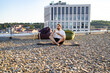 © sofiko14 - A man with a beard sits cross-legged on a yoga mat on a gravel rooftop terrace, eating from a bowl while beanbag chairs and a modern building are visible in the background