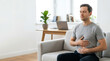 © Sofia - Man practicing deep breathing or meditation at home. Male experiencing stomach pain or discomfort in a modern living room. Copy space for text