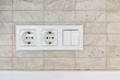 © reddish - White power outlets and light switches on a textured tiled wall
