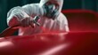 © 69 - Man in protective suit and mask spray painting red car surface in workshop with professional equipment close-up detail of automotive paint application process