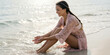 © Aleksei Solovev - Sitting on the sand with one braid, smiling and holding her braided hair, a young woman wears a pink lace dress and pearl necklace near the ocean waves.