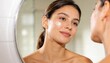 © Future Vision - Applying woman showing bare shoulders touching cream dab on cheek at bathroom vanity, round mirror