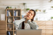 © 220 Selfmade studio - Young asian woman feeling severe pain in her neck looking very stressed and tired while doing work at home office desk with laptop. Exhausted female massaging tense muscle working remote