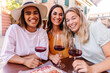 © Xavier Lorenzo - Happy multiracial women drinking red wine at cafe table. Young female friends enjoying relaxed social time in European city. Lifestyle and social concept.