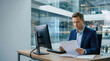 © spyrakot - Professional in glass - walled office reviewing plain paperwork
