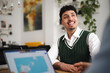 © Studio Marmellata - A young man smiles while looking up during a meeting. He is wearing a white shirt and a green sweater vest.