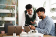© Studio Marmellata - Two young men collaborate on a project, one showing the other something on a mobile device while laptops are on the table.