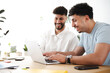 © Studio Marmellata - Two young men collaborate on a project, smiling as they work together on a laptop at a desk with office supplies.