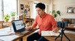 © Image - A man working from home using a laptop and taking notes in a notebook while recording a video