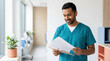 © OlgaNeuroArt - Smiling male doctor in teal scrubs reviewing a patient chart on a clipboard. Professional ethnic physician in a modern hospital hallway. Healthcare and medical documentation concept