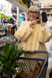 © Ivan Traimak - Happy senior woman pointing at a blank smartphone screen while pushing a shopping cart