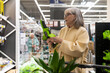 © Ivan Traimak - Mature woman examining a cordless mini chainsaw, considering her purchase in a retail store