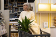 © Ivan Traimak - Woman pushing a shopping cart with a plant in a retail store aisle