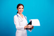 © deagreez - Cheerful female doctor in white coat smiles while presenting a paper document against a bright blue studio background