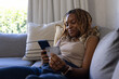 © Wavebreak Media - African woman reclining on light-gray sofa in living room, holding smartphone and payment card