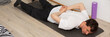 © pundapanda - A man, 53 years old, lies on a yoga mat at home, performing a stretching exercise. He focuses on his fitness routine in a simple indoor space with plants around, banner