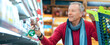 © Prostock-studio - A man shops in a grocery store. He is looking at items on the shelf while holding a shopping cart. The store has various products visible in the background.