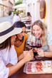 © Xavier Lorenzo - Young female friends enjoying red wine outdoors at cafe table. Multiracial women sharing friendship and leisure in European city. Lifestyle and travel concept.
