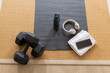 © Wavebreak Media - Black dumbbells are resting on gray exercise mat in home workout, with green bottle and headphones