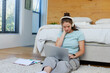 © Wavebreak Media - Woman sitting on shag rug at foot of bed in bedroom, wearing headphones, using silver laptop
