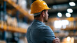 © Laura - Confident industrial worker standing in a factory warehouse, strong professional presence, manufacturing environment, hard hat and safety gear, faceless, back to camera, defocused