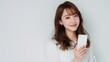 © Flower images - スマートフォンを持って微笑む若い女性のポートレート。SNSやコミュニケーション関連の広告や記事に最適なイメージ素材