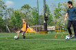 © chokniti - World cup concept with soccer ball or football player, young boy practicing soccer on outdoor field with coach, training cones and hurdles in sunny park