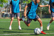 © chokniti - World cup concept with soccer ball or football player, young boy kicking soccer ball on grass field with teammates in blue training bibs outdoors