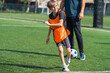 © chokniti - World cup concept with soccer ball or football player, young boy on soccer field in orange vest with coach, outdoor practice, sunny day