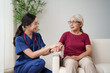 © Tj - Young Asian nurse discussing health with an elderly woman at home, holding her hand while providing support and conveying empathy during the healthcare visit