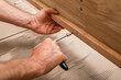 © valiantsin - Hands tighten a screwdriver on a wooden furniture panel. Close up of manual assembly and repair work. Home improvement, DIY, and joinery task..