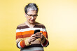 © Petro - Senior woman wearing glasses and striped sweater, actively engaging with her smartphone. She is focused on the device