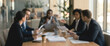 © Vhagar - A diverse group of business professionals engaged in a meeting around a conference table, discussing documents and ideas in a modern office setting.