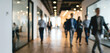 © Vhagar - A busy office corridor filled with professionals walking and engaging in their work environment, showcasing modern architecture and bright lighting.